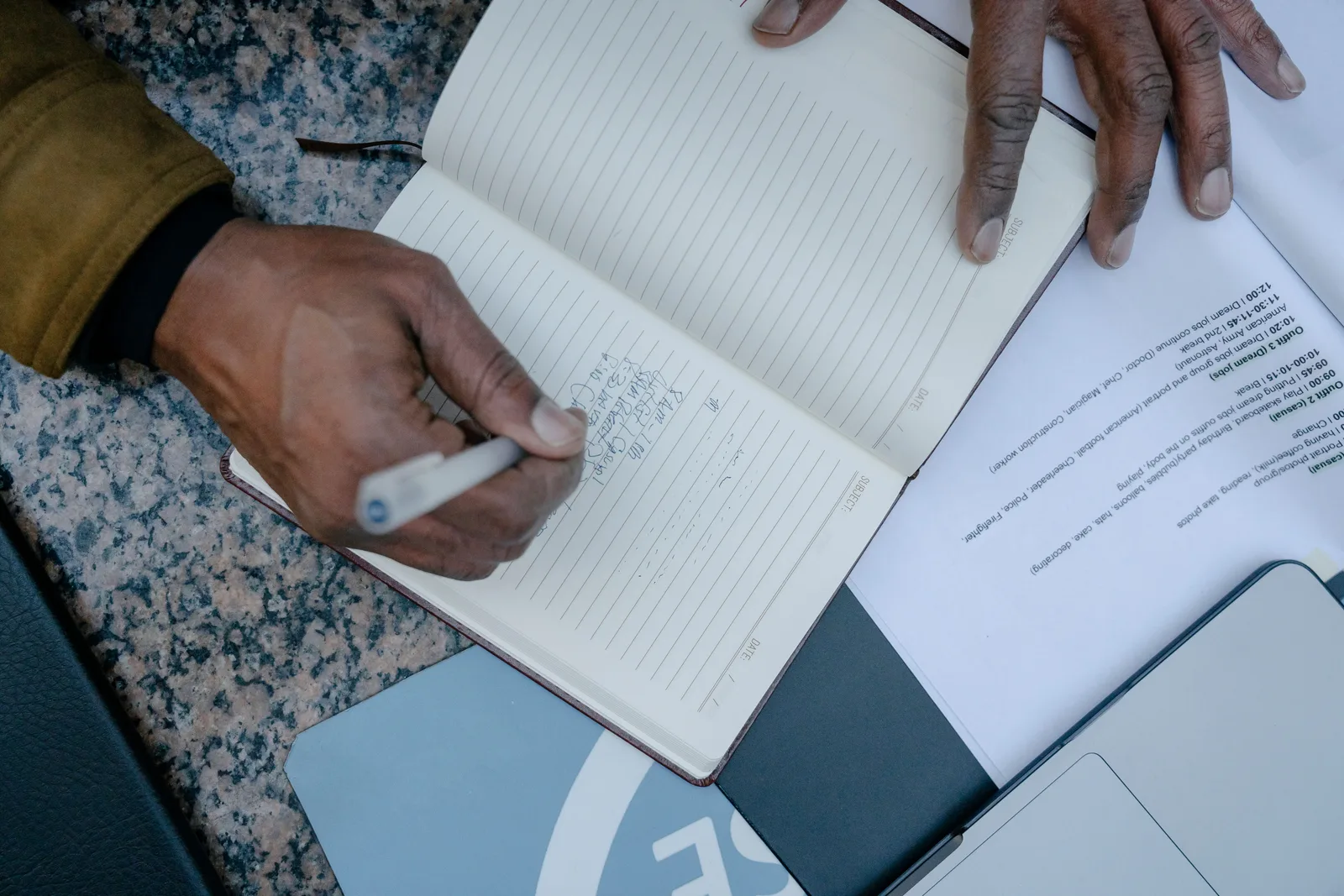 Top view of a person's hand writing in a notebook amidst business documents, focusing on handwriting. Business quotes misquotes: how to check a quotation