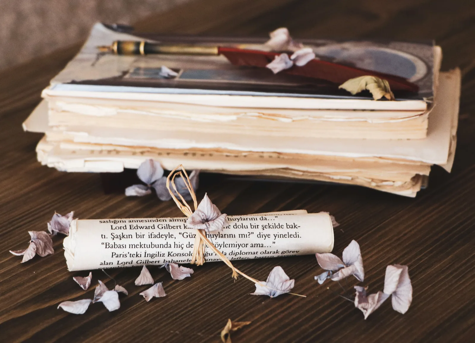 Stack of vintage books with a quill pen and scattered paper flowers on a wooden table. Life quotes context: signal versus noise