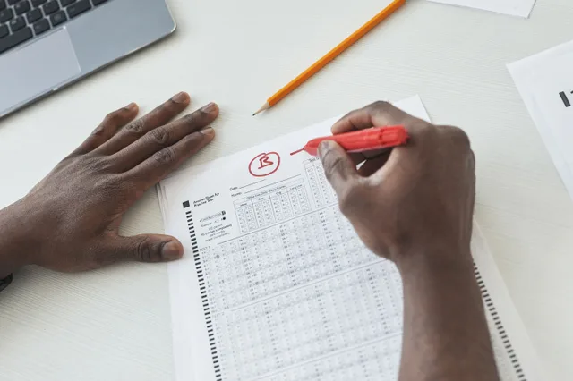 Close-up of a teacher grading multiple choice exams with a red pen on a desk. Misquotes and fact checks analysis: a grading scale